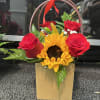 Red roses and a sunflower in a gold gift bag with a red ribbon