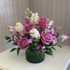 Pink roses and purple orchids arranged in a green glass vase