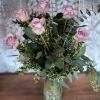 Lavender roses arranged in a clear glass vase with mixed greenery