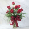 Red roses arranged in a glass vase with a burgundy ribbon