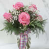 Pink roses in a glass vase with baby's breath and a plaid ribbon