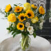 Yellow roses and sunflowers arranged in a clear glass vase