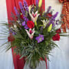 Tall bouquet of red roses, purple flowers, and white lilies in a glass vase