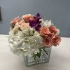 Pink roses and white hydrangeas in a clear square vase with purple orchids