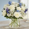 White roses and blue flowers arranged in a clear glass vase