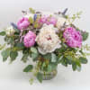 Low glass vase arrangement with pink and white blossoms and purple accents in a loose, full design