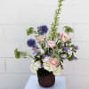 An artistic, garden-inspired arrangement featuring airy ranunculus, delicate clematis, textured allium, and