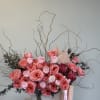 Pink floral arrangement in a white vase with tall curly branches