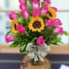 Arrangement of bright pink roses and yellow sunflowers in a glass vase with a patterned ribbon bow