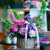Pink and purple flower arrangement in a wicker basket with a white ribbon
