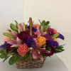 A radiant mix of peach lilies, vibrant orange roses, purple fillers, and