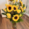 Tall vase arrangement of yellow sunflowers and yellow roses with a small card.
