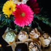 Bright gerbera daisies in a vase above assorted cupcakes