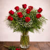 Red roses arranged in a clear glass vase with a single rose on the table