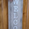Wooden welcome sign with a black-and-white bow and bee ribbon