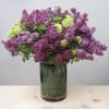 Tall arrangement of purple and light green blossoms in a clear glass cylinder vase with green lining.