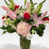 Tall arrangement of pink lilies, red roses, and white flowers in a clear glass vase