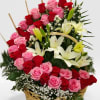 Basket arrangement of pink and red roses with white lilies and small white filler flowers.