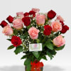 Arrangement of red and pink roses with white filler flowers in a glass vase with a red bow