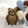 Teddy bear balloon surrounded by blue, brown, white, and clear balloons