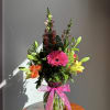 Tall mixed bouquet with pink gerbera daisy, orange roses, lilies and snapdragons in a clear vase with pink bow