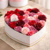 A white heart-shaped gift box overflowing with roses in red, blush pink
