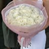 Large round bouquet of white roses wrapped in pale pink paper, held by a person in a white dress