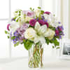Bouquet of white lilies, cream roses, and purple flowers in a clear glass vase