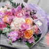 Bouquet of pink, peach, and lavender flowers wrapped in pale purple paper