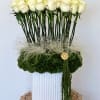 Tall arrangement of white roses in a white vase with green moss