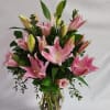 Pink lilies arranged in a clear glass vase with greenery