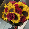 Bouquet of yellow sunflowers and red roses wrapped in black paper with gold trim.