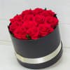 Round black box filled with red roses and wrapped with a cream ribbon