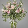 Tall arrangement of pale pink roses and lisianthus with baby's breath in a clear glass vase tied with a ribbon.