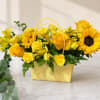 Bright yellow roses and cheerful sunflowers spill from a gold textured basket