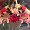 A compact woven basket overflowing with large pink roses, pale lilies, white