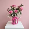Pink roses arranged in a vase with baby's breath and a pink ribbon