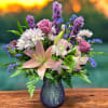 Mixed bouquet of pink lilies, roses, and white daisies in a blue vase