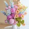 Colorful bouquet of pink, blue, and peach flowers in a white vase