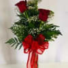 Red roses arranged in a clear vase with a large red bow
