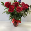 Red roses with white and purple filler flowers in a red vase with a red ribbon bow