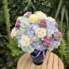Bouquet of pastel roses and blue hydrangeas in a dark vase