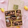 Box of assorted chocolates with yellow tulips on a pink background