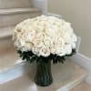 Large arrangement of white and cream roses in a clear glass vase on marble steps