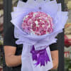 Bouquet of pink roses wrapped in lavender paper with a purple ribbon