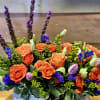 Orange roses and purple flowers in a low rectangular arrangement