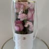 Soft pink roses and pale carnations rise from a tall white cylindrical