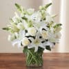 Arrangement of white lilies, roses, and snapdragons in a clear glass cylinder vase