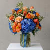 Bouquet of blue hydrangeas, orange tulips, and peach roses in a glass vase