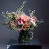Soft, garden-fresh blooms spill from a dark glass pitcher vase to create